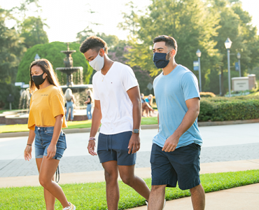 One female and two male students wearing masks walking on campus