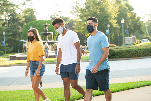 One female and two male students wearing masks walking on campus